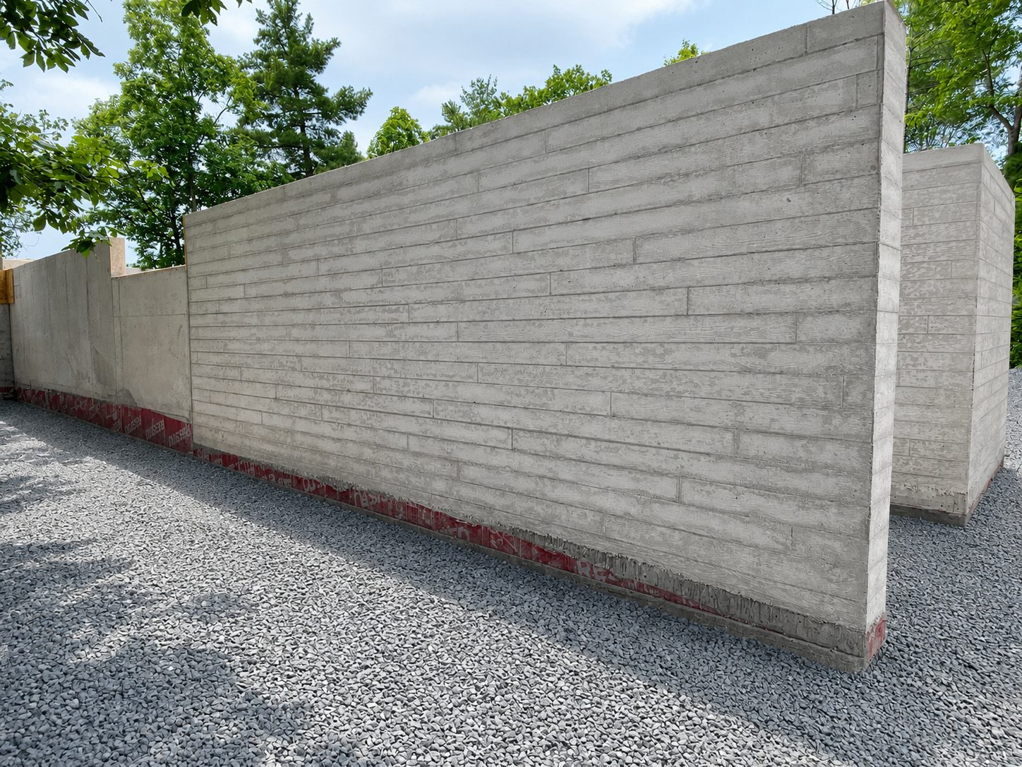Board-formed concrete walls with wood-grain texture over waterproofed base and gravel plane