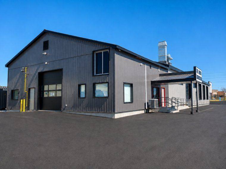 A completed steel-clad commercial shop and office building under a clear sky, with paved apron and covered entry