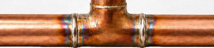 A soldered copper tee, the metal discoloured blue and purple around each joint from torch heat