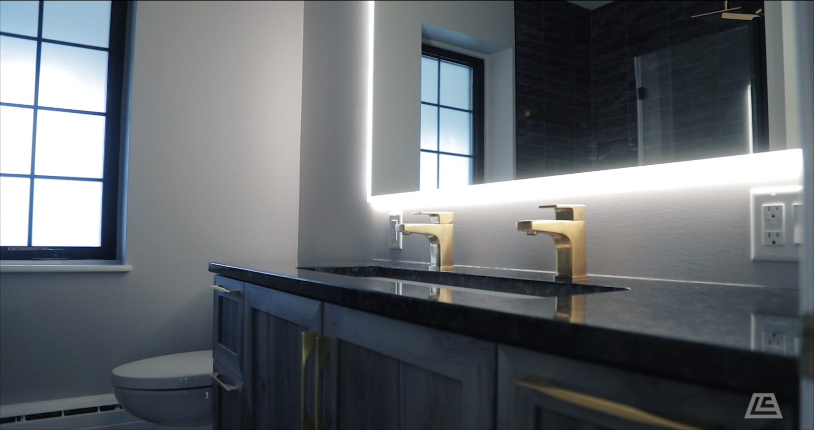 Granite-topped double vanity with brass faucets and backlit mirror