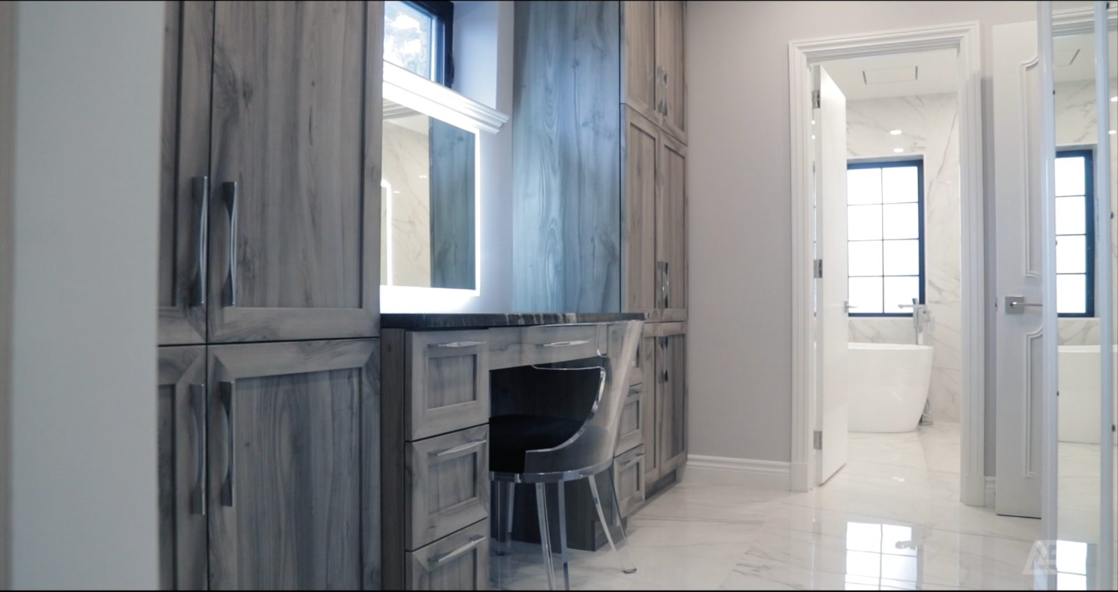 Dressing suite vanity with backlit mirror and marble floor, tub beyond