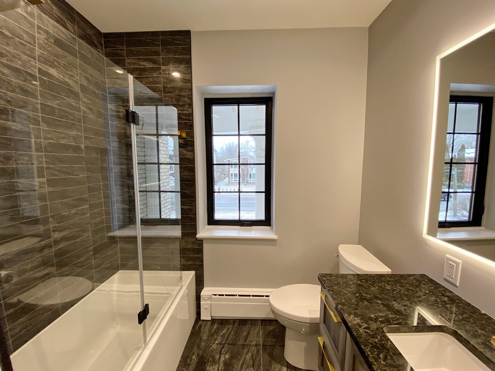 Guest bath with dark stone tile, glass shower screen and brass accents