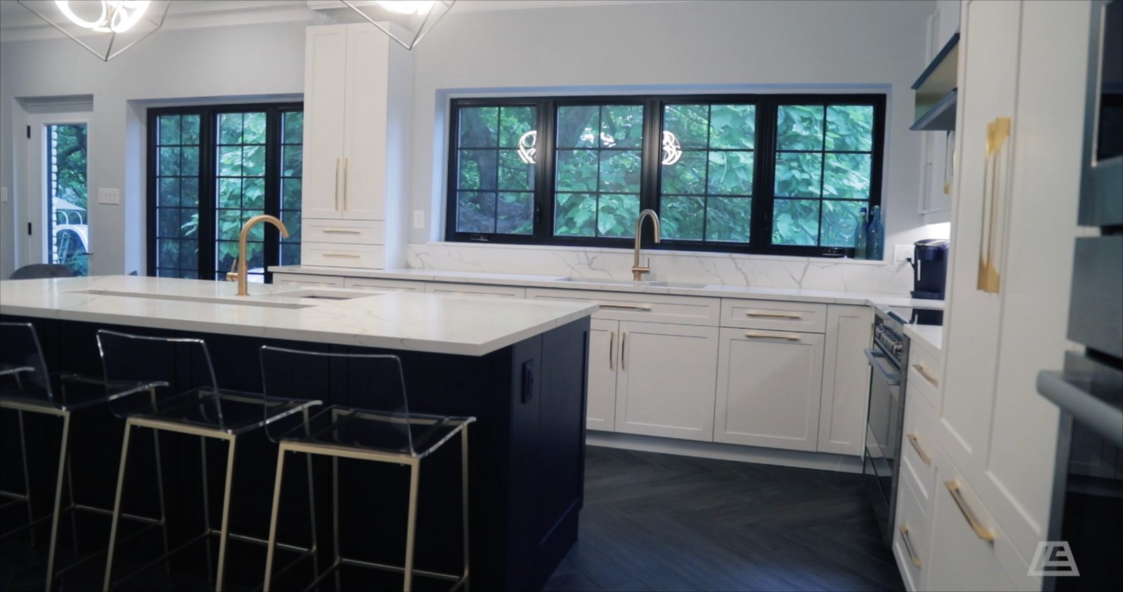Navy island and brass faucets under black grid windows to the garden