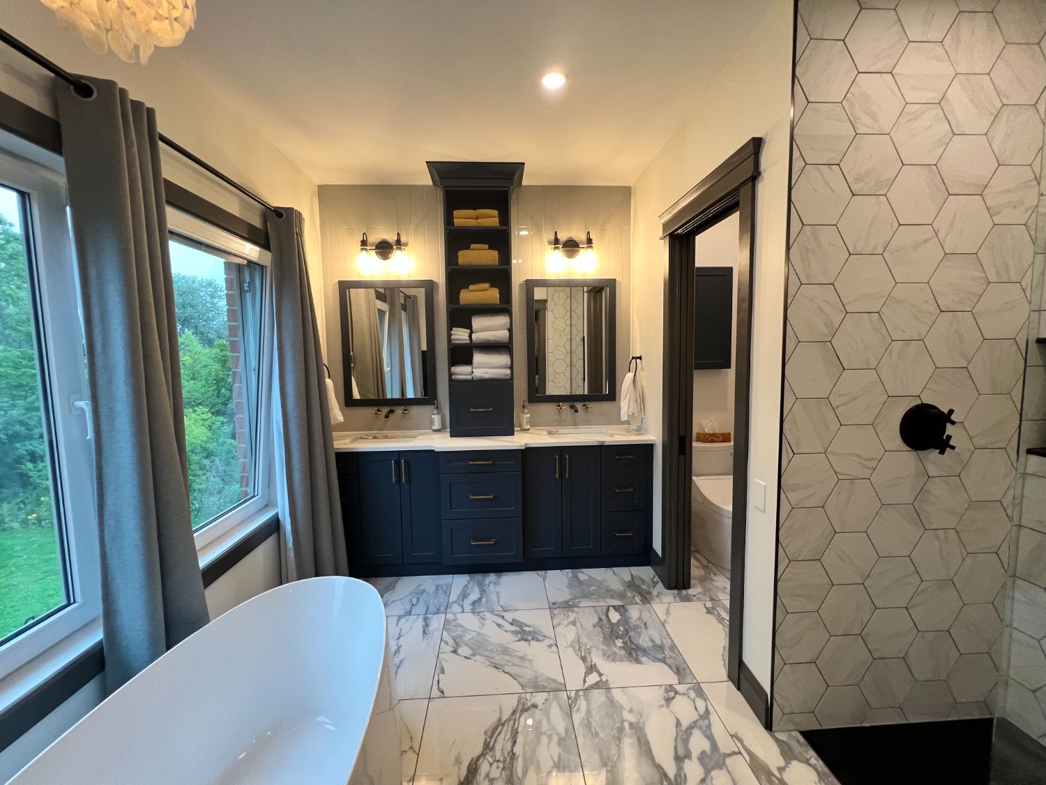 Primary bath with navy double vanity, marble floors and freestanding tub