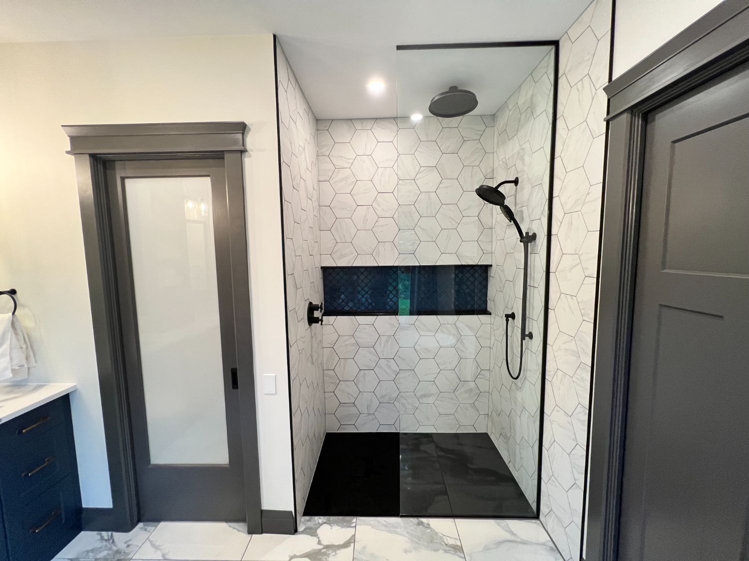 Walk-in shower in marble hex tile with a blue arabesque niche