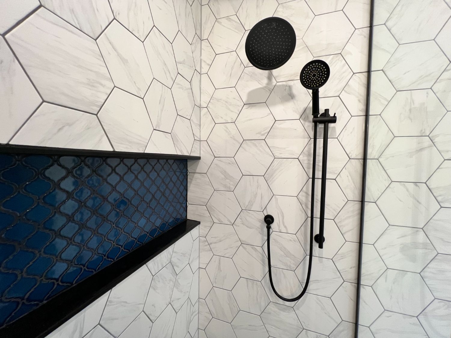 Detail of marble hex tile and glossy blue niche with black fixtures
