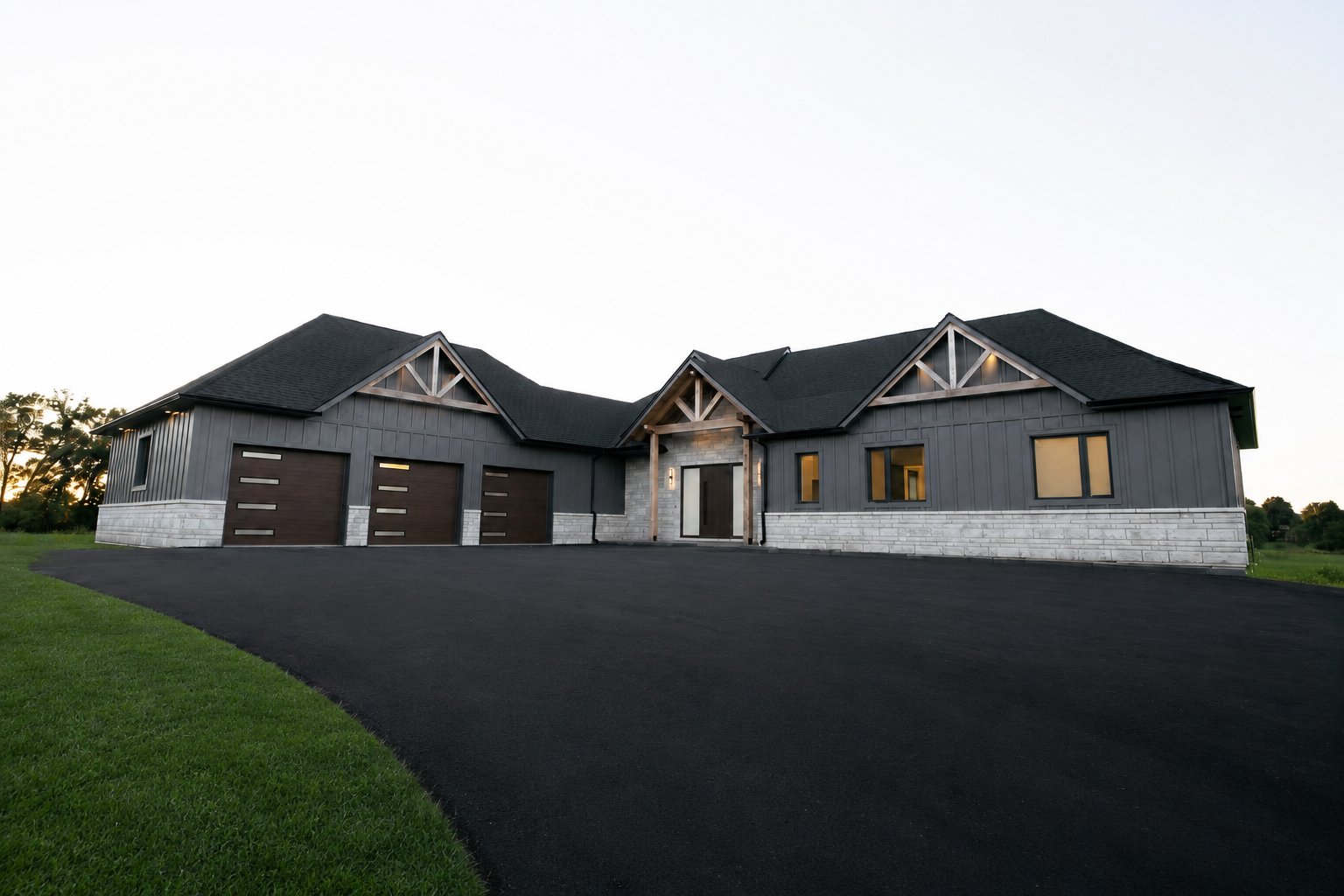 Dark board-and-batten ranch with timber-truss gables, stone base and triple garage at dusk