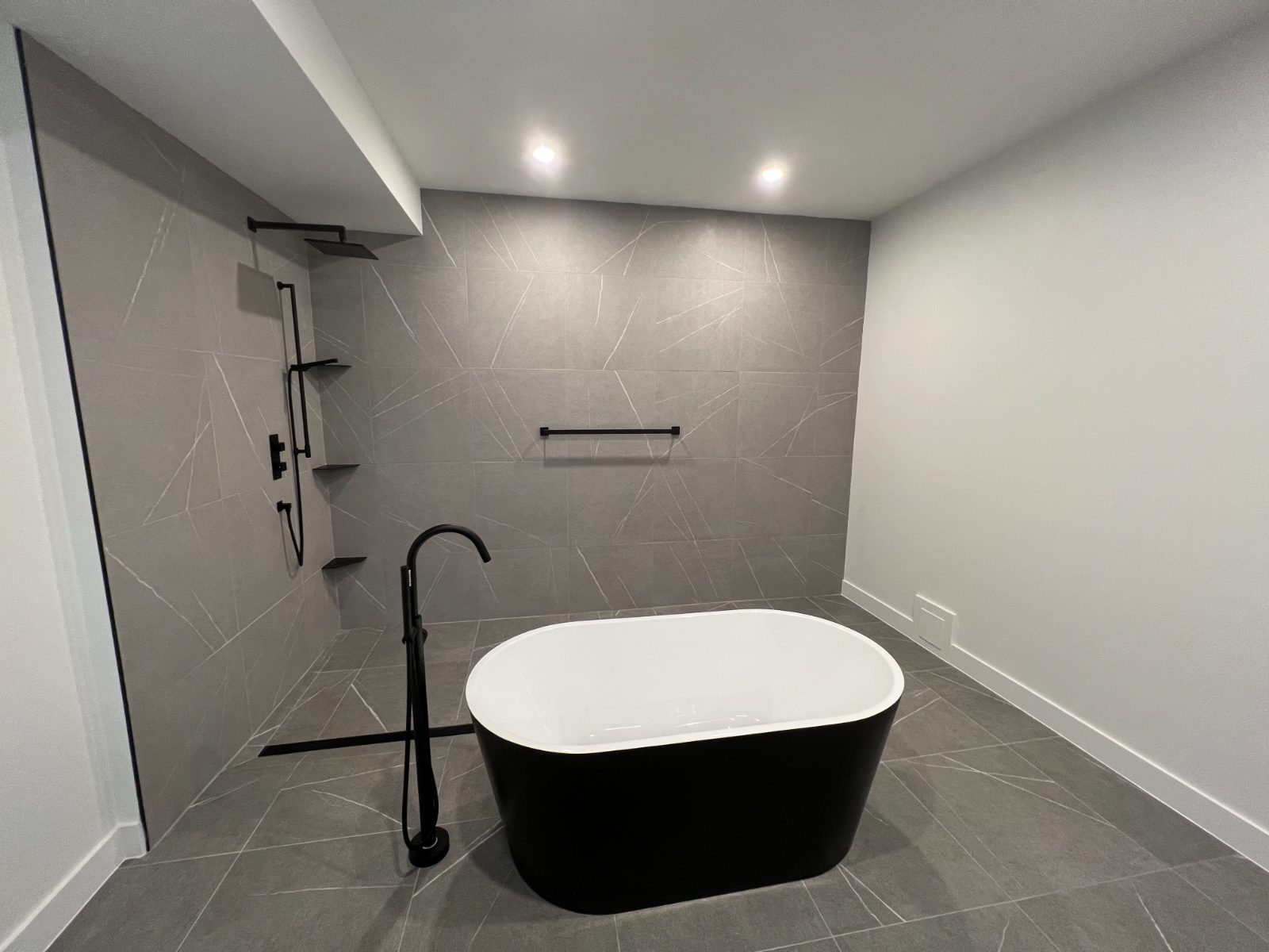 Black freestanding tub and open grey-tile shower on the walkout level