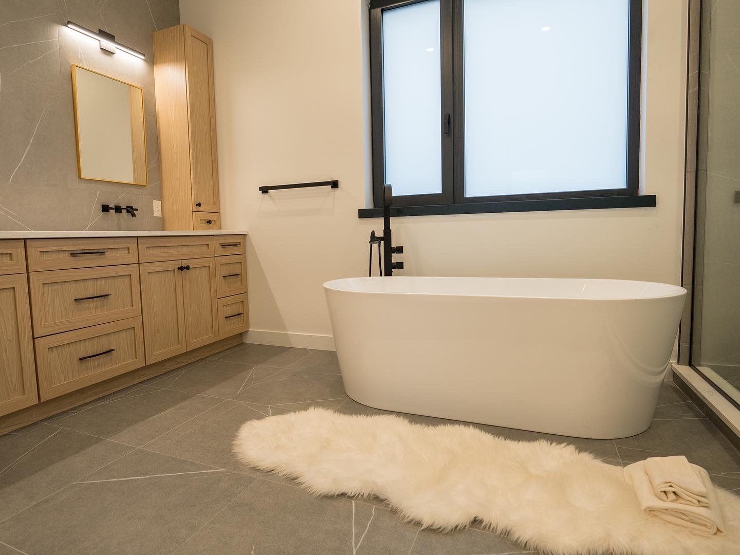 Freestanding tub under a frosted window beside the white-oak vanity