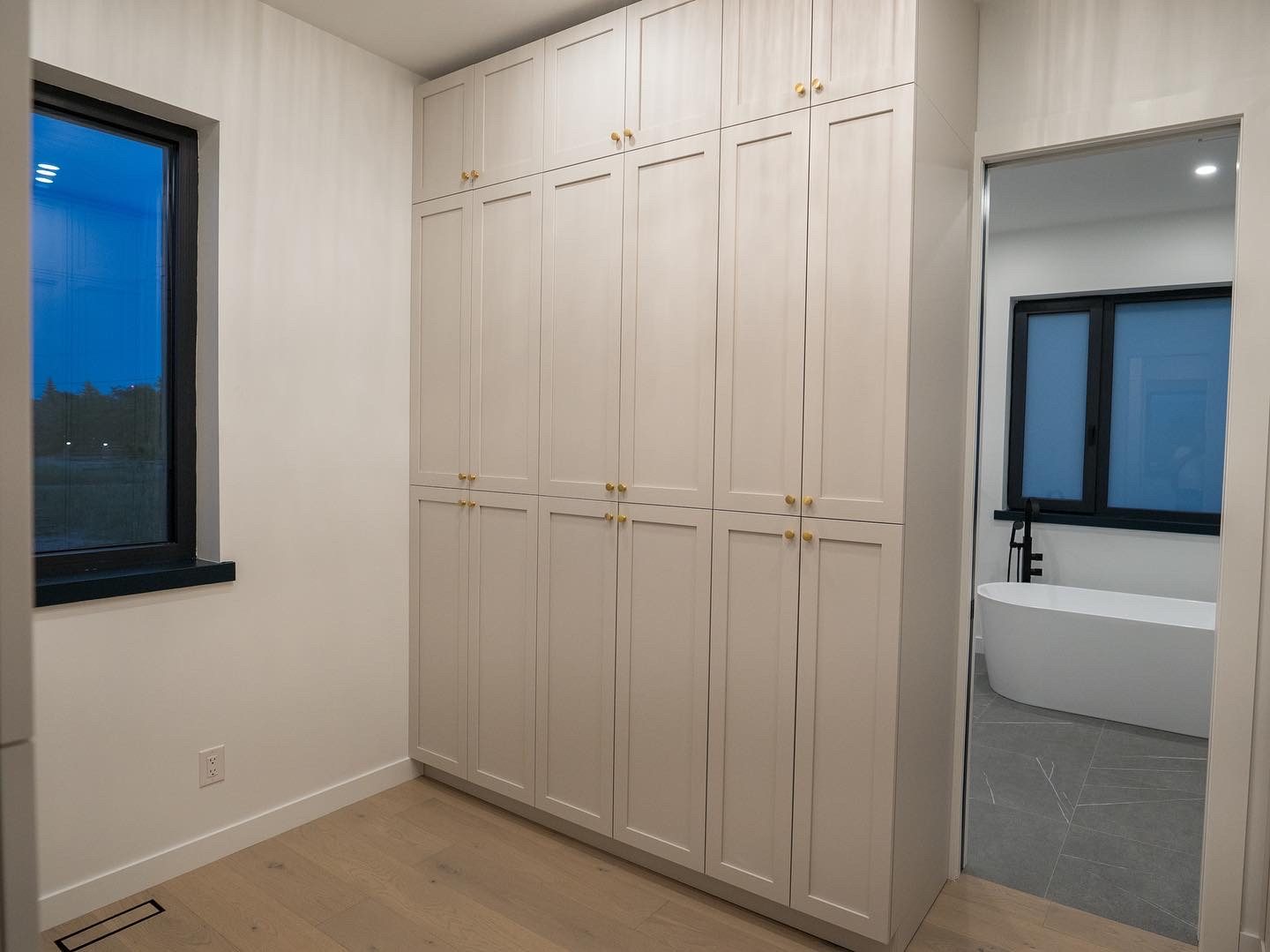Floor-to-ceiling wardrobe wall in warm white with brass knobs, bath beyond