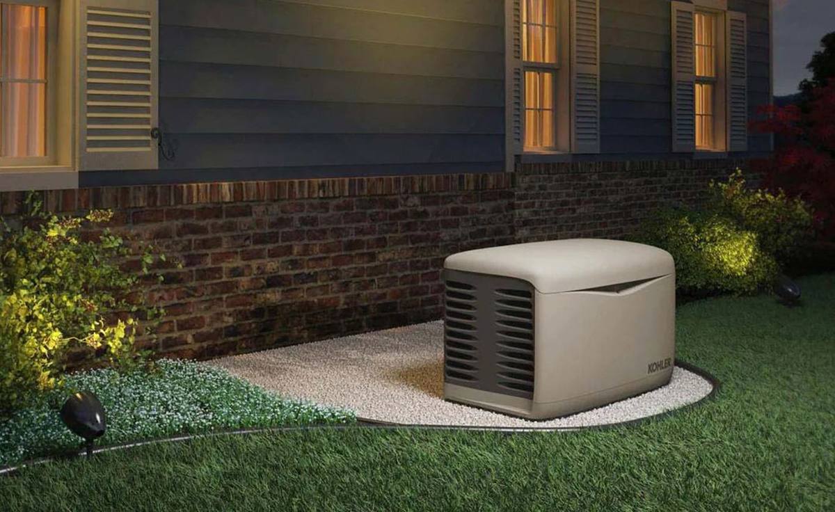 A Kohler standby generator on a gravel pad beside a house at dusk