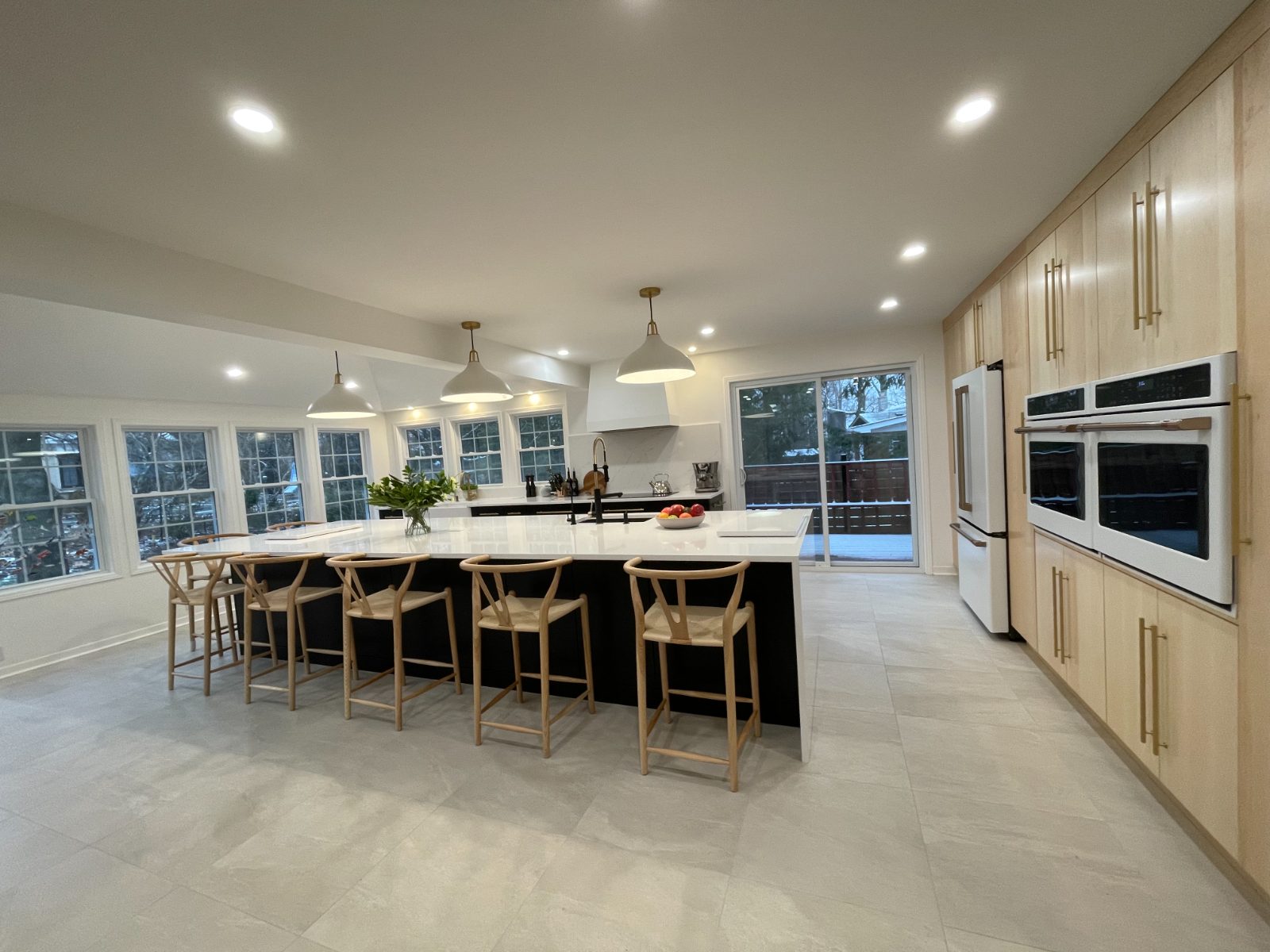 Open kitchen with black island, wishbone stools and floor-to-ceiling maple cabinets
